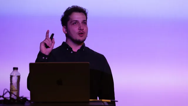 Jeb on stage at Webdevcon 2024, gesturing mid-sentence under purple light