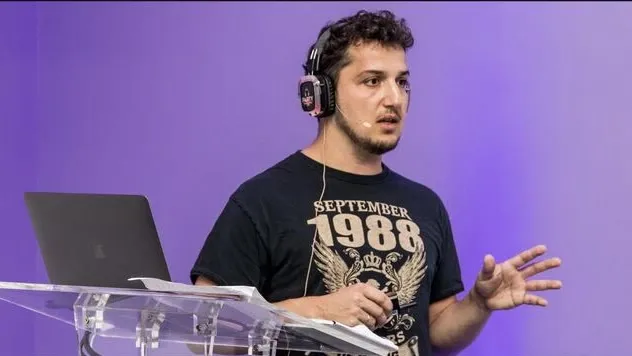 Jeb on stage at Wix DevCon 2022 in a headphone mic, gesturing beside a clear lectern with a laptop, under purple light